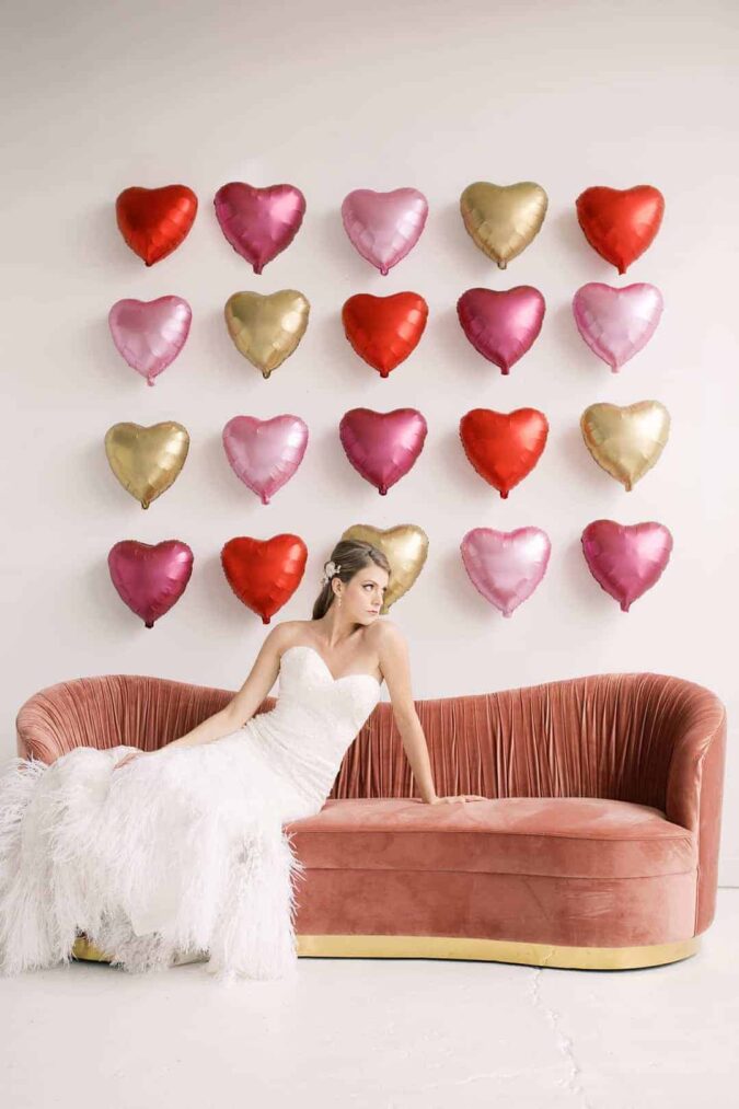 Valentines Day wedding inspiration, featuring giant heart balloon backdrop and romantic feather wedding dress